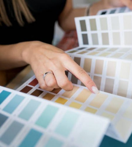 Close-up of two women choosing samples of wall paint. Interior designer consulting a client looking at a color swatch. House renovation concept