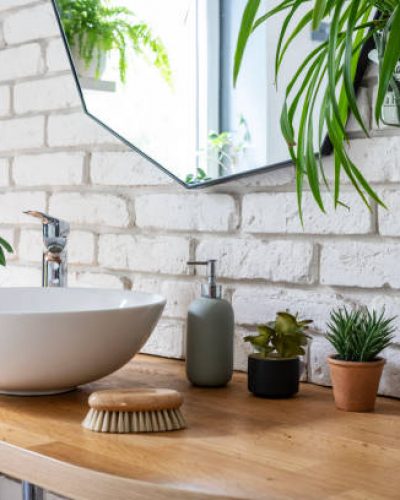 Bright modern interior of bathroom with green colour of plant, ceramic bathroom sink and mirror on the white brick wall at home in real estate.